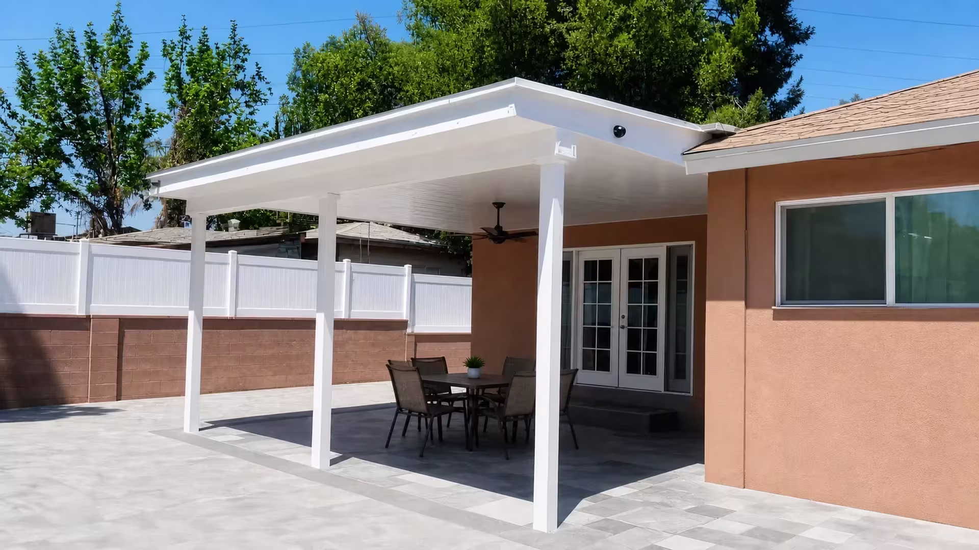 Peach stucco walls rise behind a White vinyl cover, its fascia meeting a brown masonry wall topped with fencing