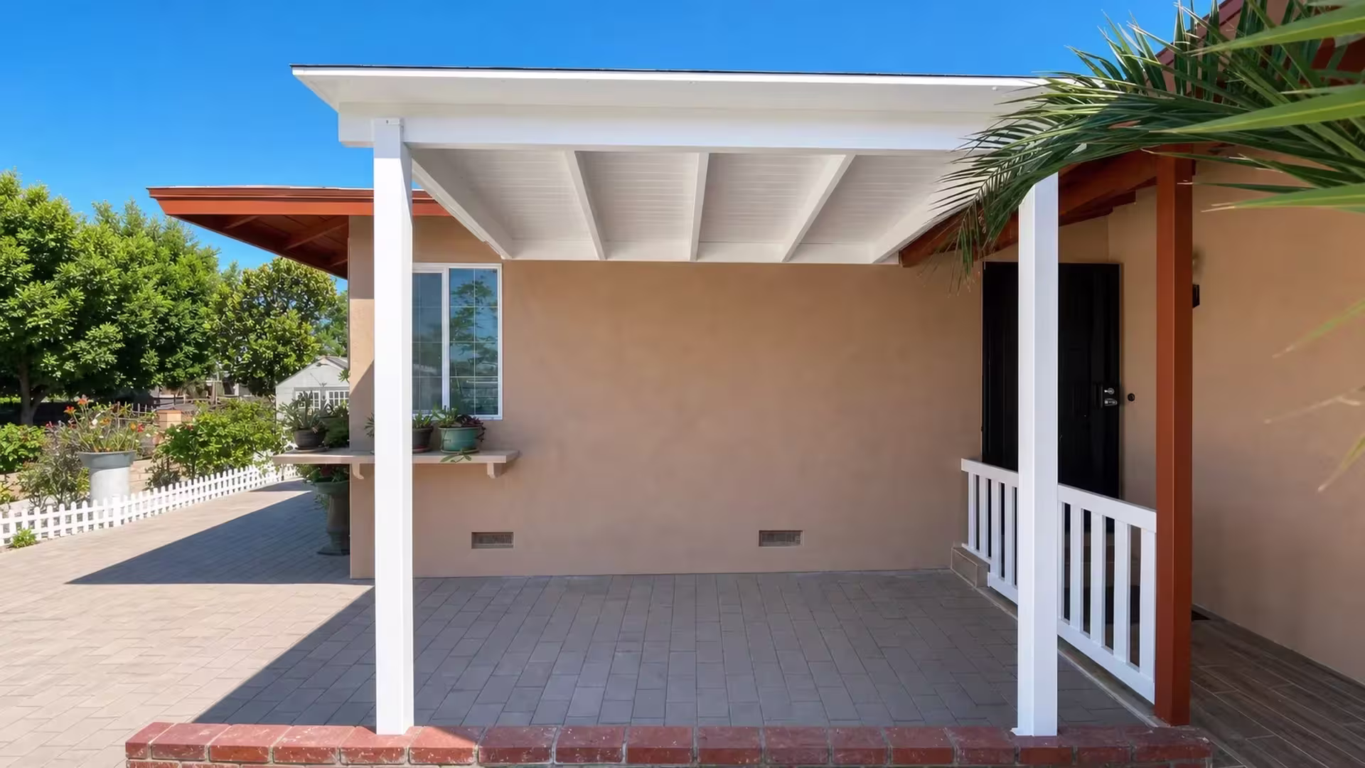 A matching White railing edges the brick bordered slab next to this vinyl cover and a neighboring brown one