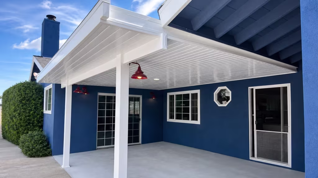 A chimney and octagonal window sit along dark blue siding, framed by the White vinyl cover and a hedge