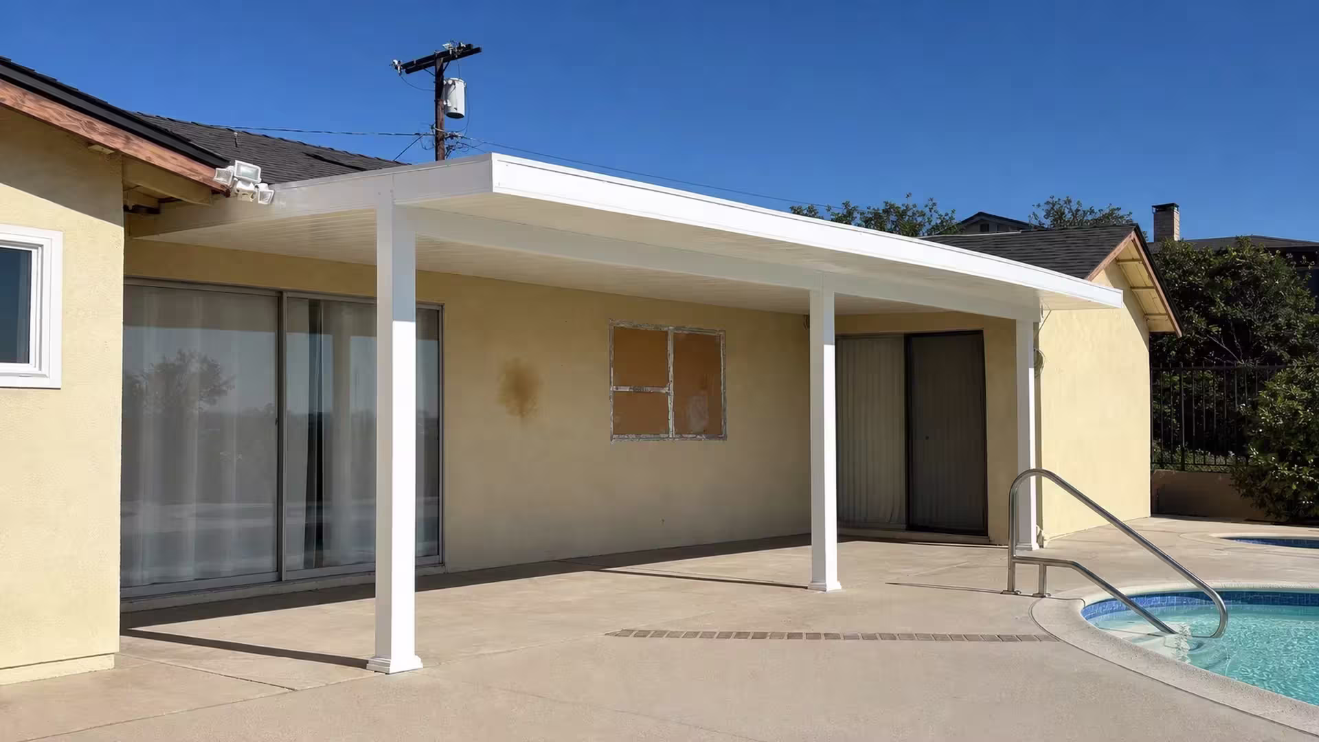 Metal handrails trace the pool deck edge beneath the White vinyl cover mounted on pale yellow stucco walls