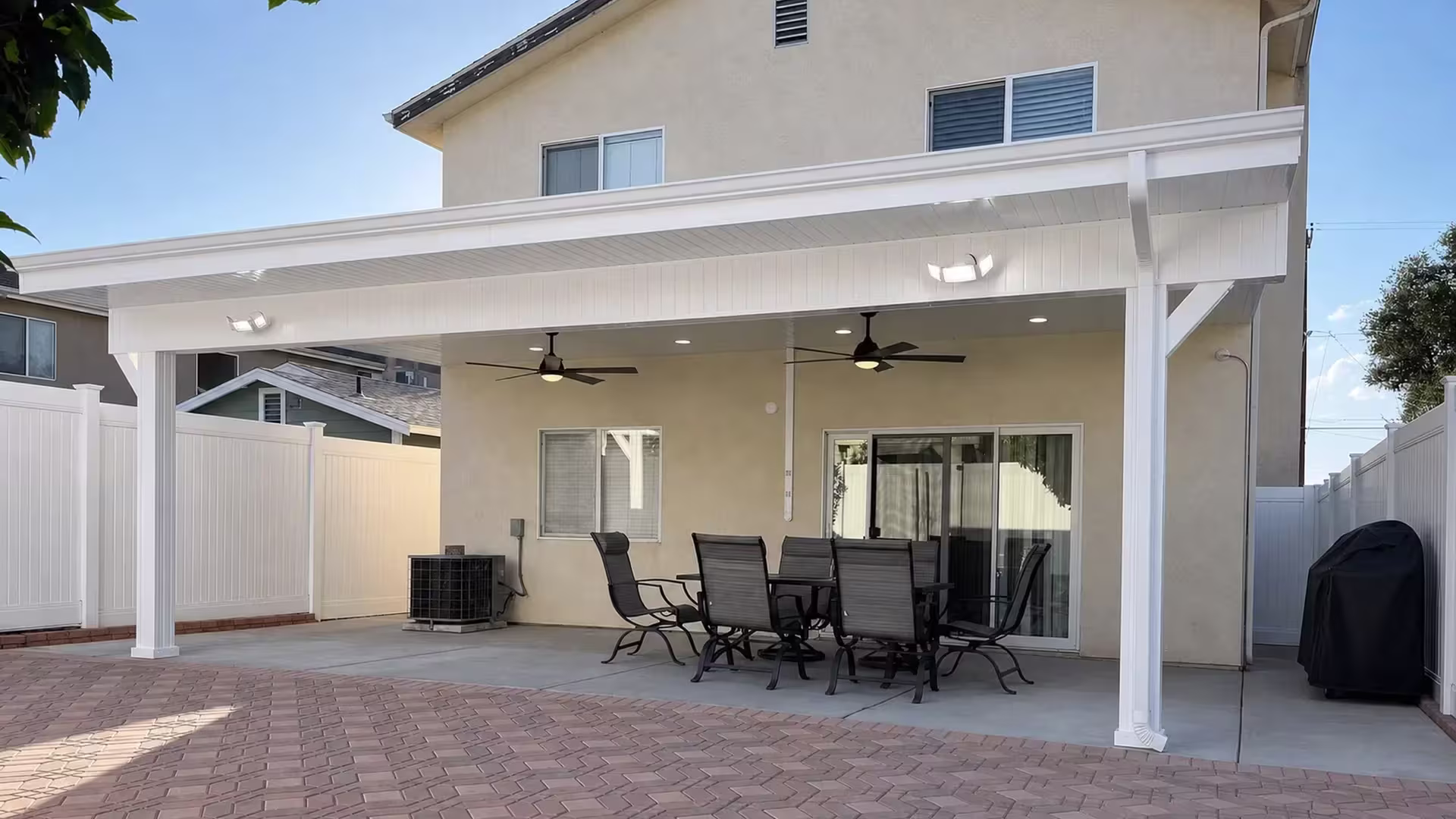 Two ceiling fans and recessed lights hang beneath the White vinyl cover at a two story stucco home with diagonal braces