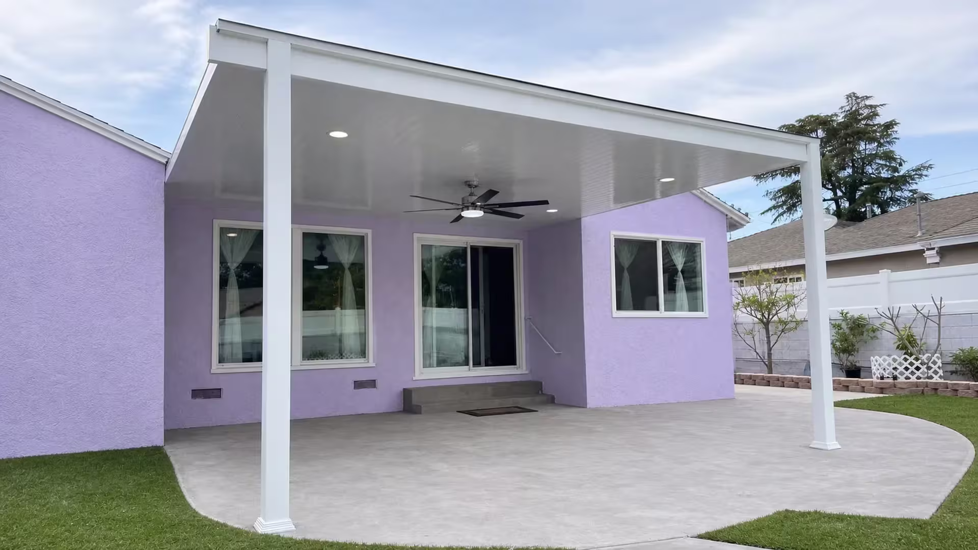 A side yard fence and neighboring trees frame the White vinyl cover set over a concrete patio slab
