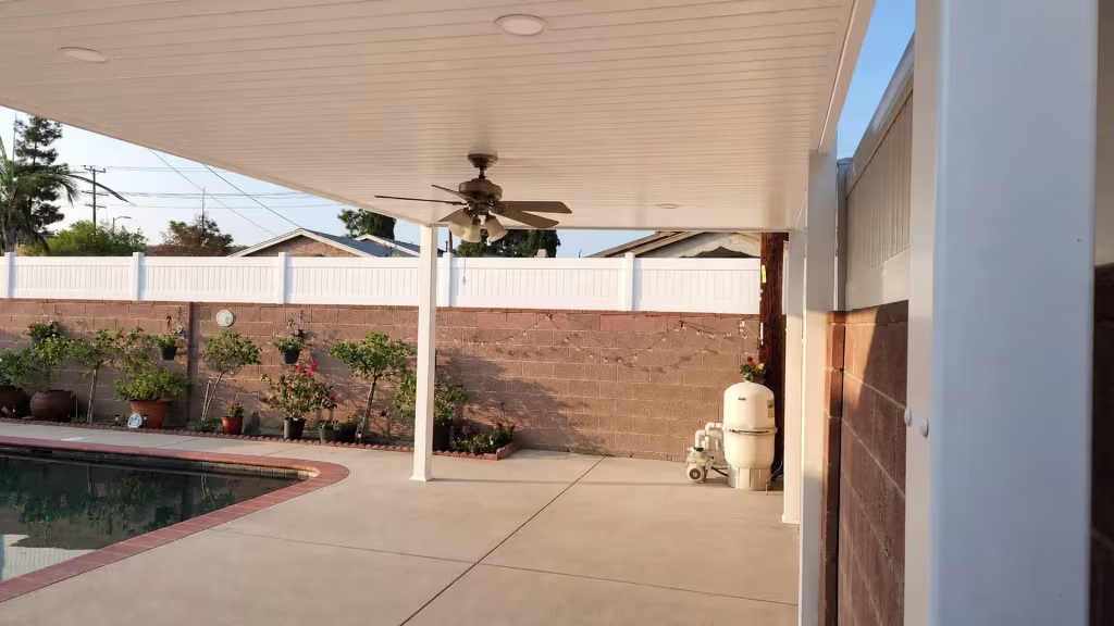 Pool equipment and plumbing sit close to the White vinyl cover shading a concrete deck beside brown masonry walls