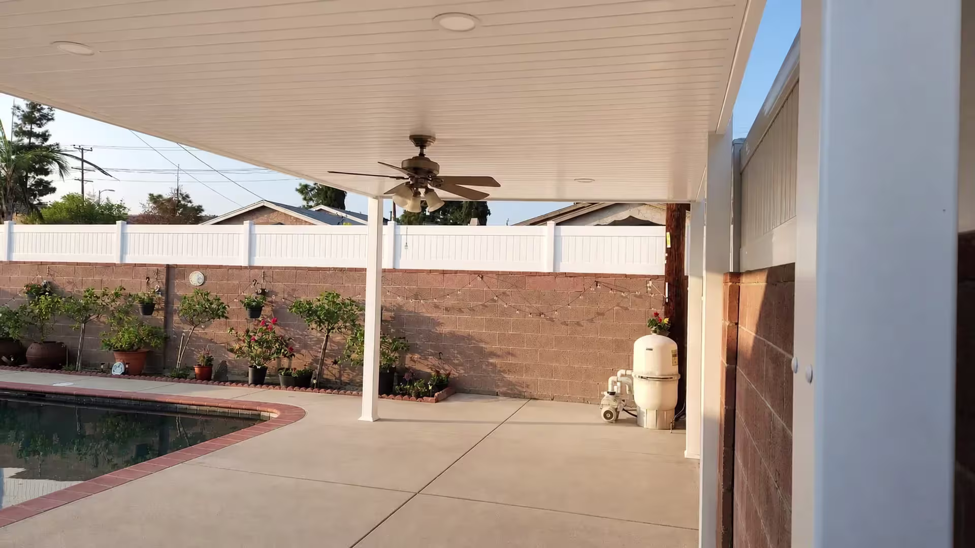 Pool equipment and plumbing sit close to the White vinyl cover shading a concrete deck beside brown masonry walls