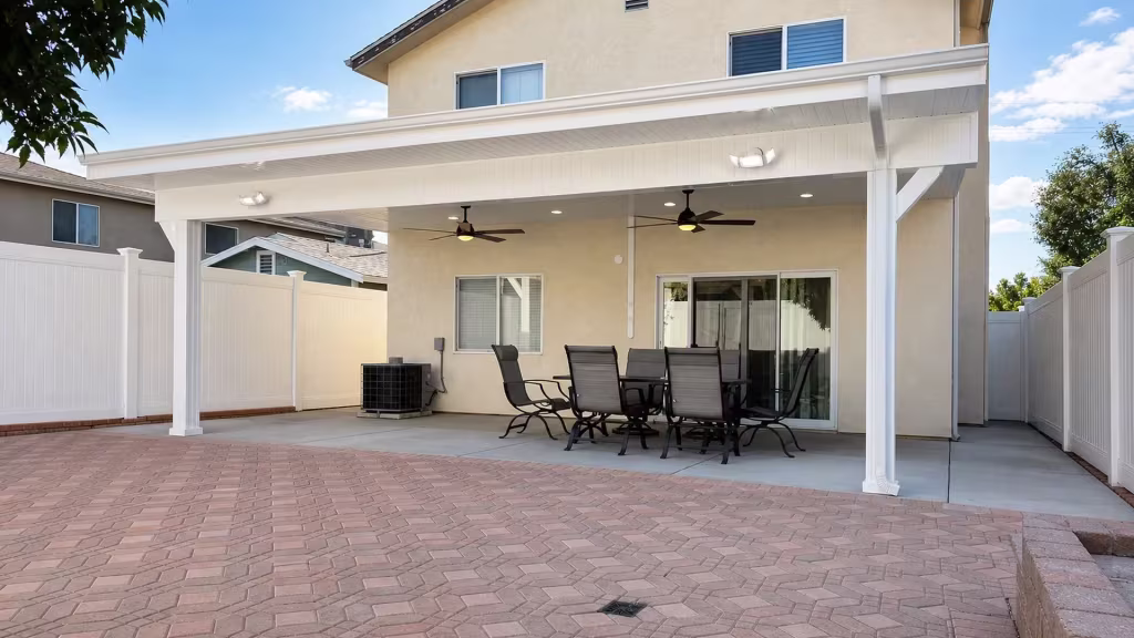 Two fluted White vinyl support posts anchor a solid patio cover beside an HVAC unit and sliding glass door
