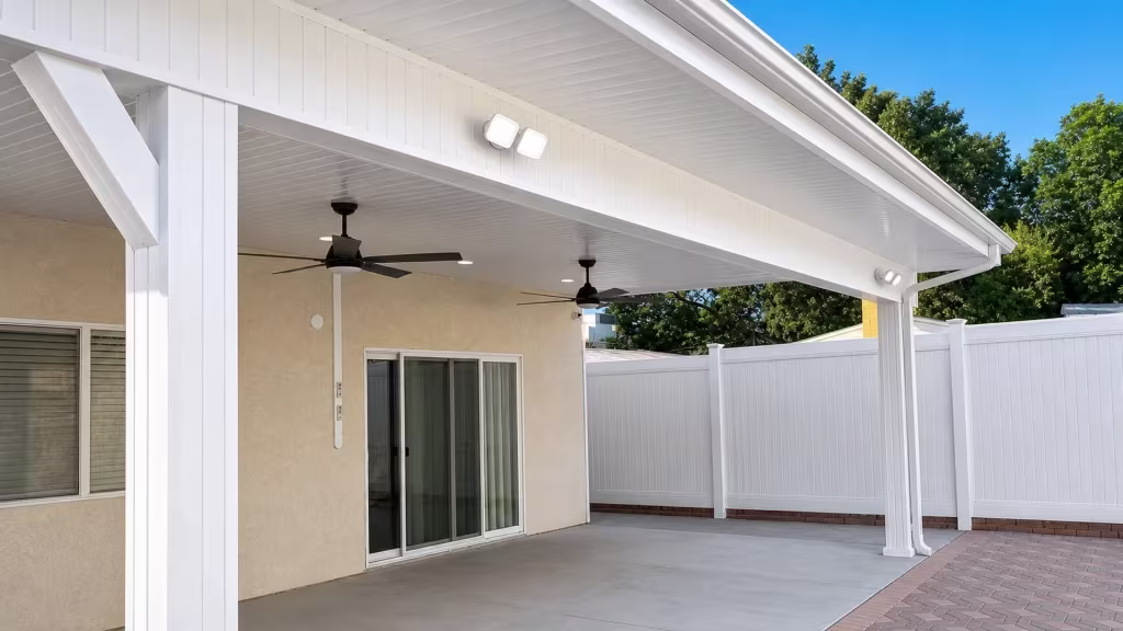 A diagonal corner brace joins the fascia where this White vinyl solid patio cover meets beige stucco near mature trees
