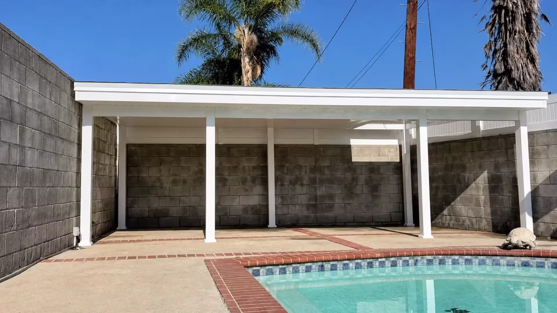 Four unequal width bays span this White vinyl solid patio cover above red brick coping around the swimming pool