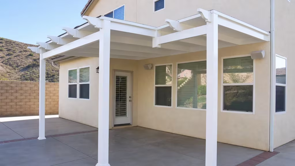 Two connected rectangular bays make up this White vinyl solid patio cover against a hillside two story stucco house