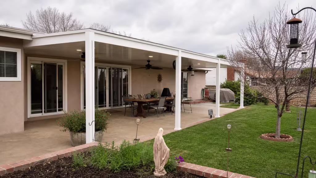 A garden statue and barbecue sit near this White vinyl solid patio cover spanning the concrete patio behind the house