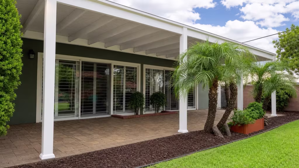 Palm fronds cluster beside one support post of the White vinyl cover extending over a brick paver patio