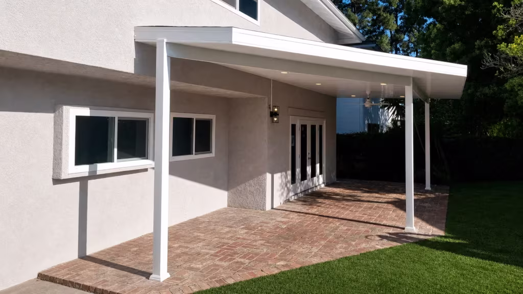 A mounted fan and recessed lights sit under the White vinyl cover above a brick paved rear yard