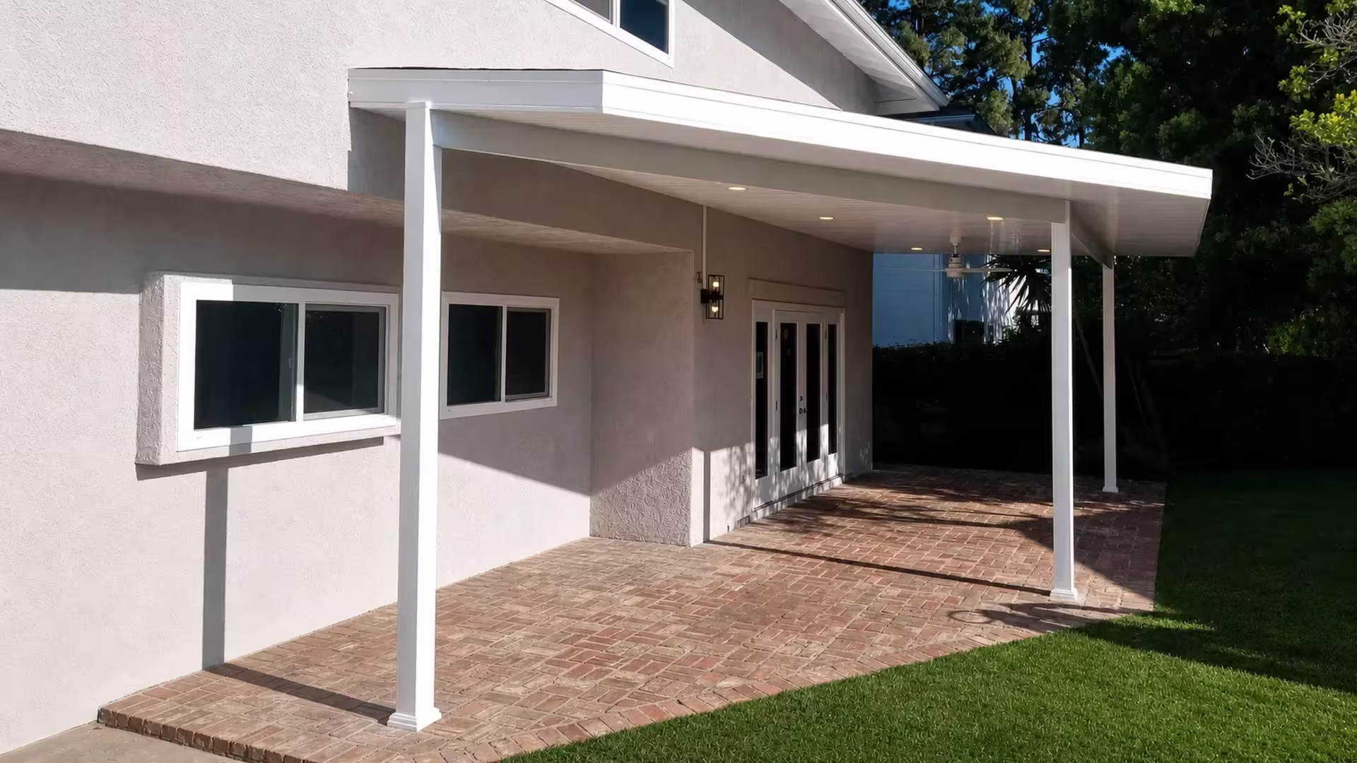 A mounted fan and recessed lights sit under the White vinyl cover above a brick paved rear yard