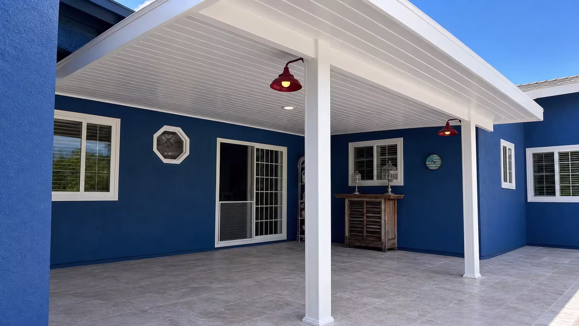 White trimmed windows border the blue exterior wall where the White vinyl cover projects over the tiled floor below