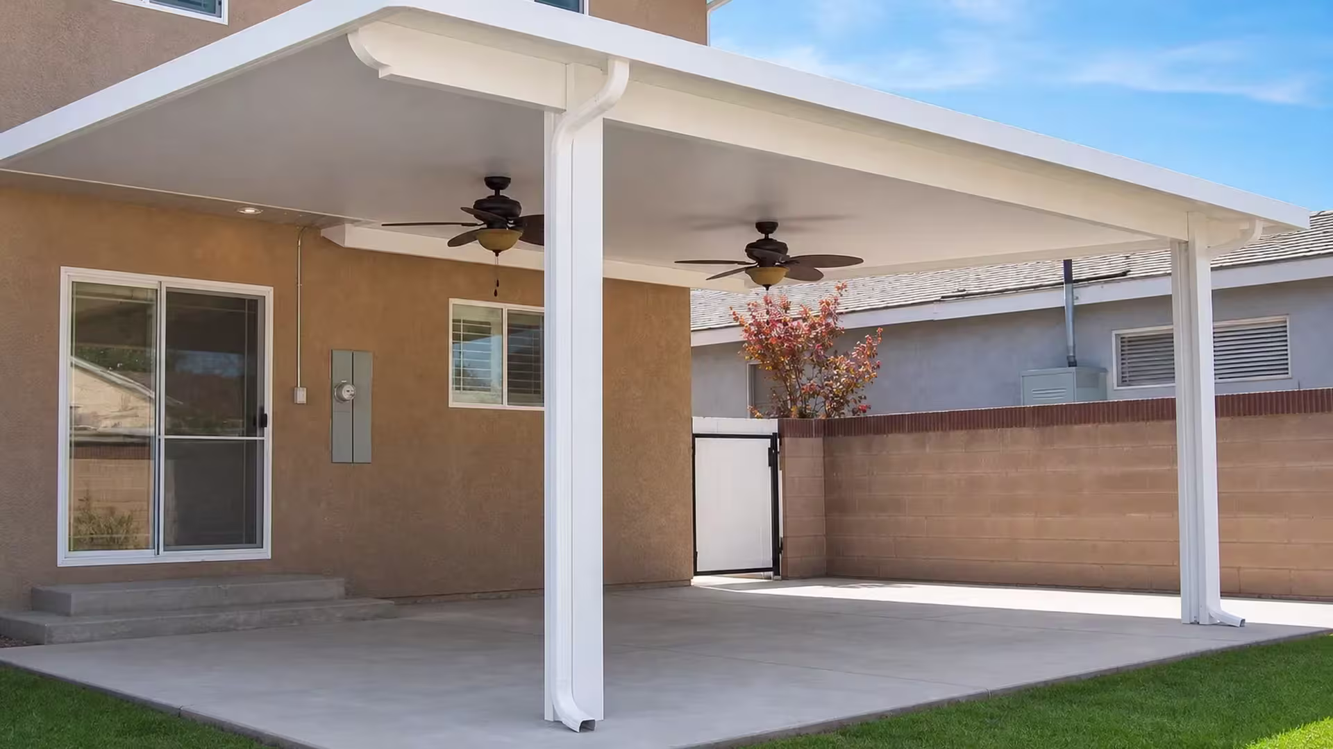 An electrical panel mounts beside the masonry boundary wall under the White vinyl cover at the tan stucco home
