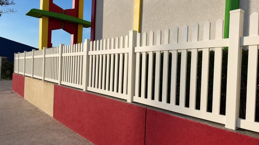 Evenly spaced Tan vinyl pickets and capped posts form a fence line along a masonry wall