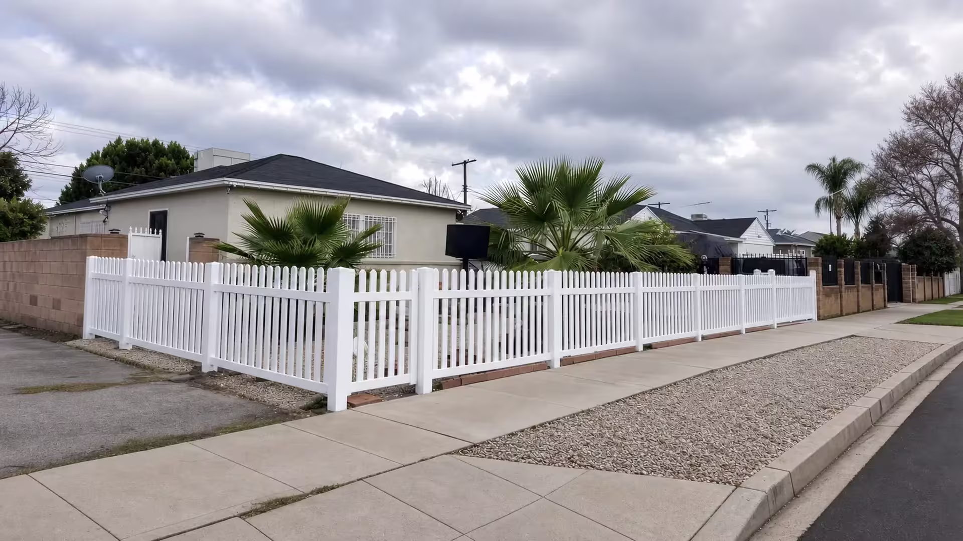 A White vinyl picket fence forms an L shape wrapping the corner of a residential lot