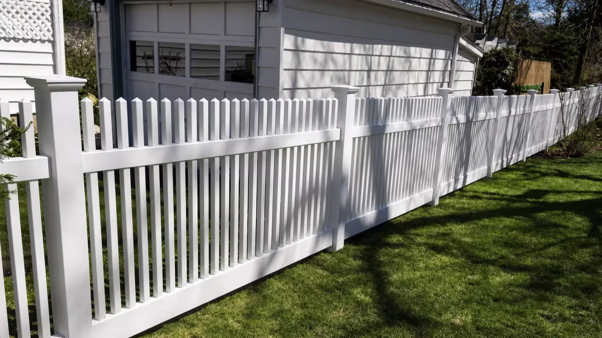 A long White vinyl picket fence stretches past a White detached garage into the distance