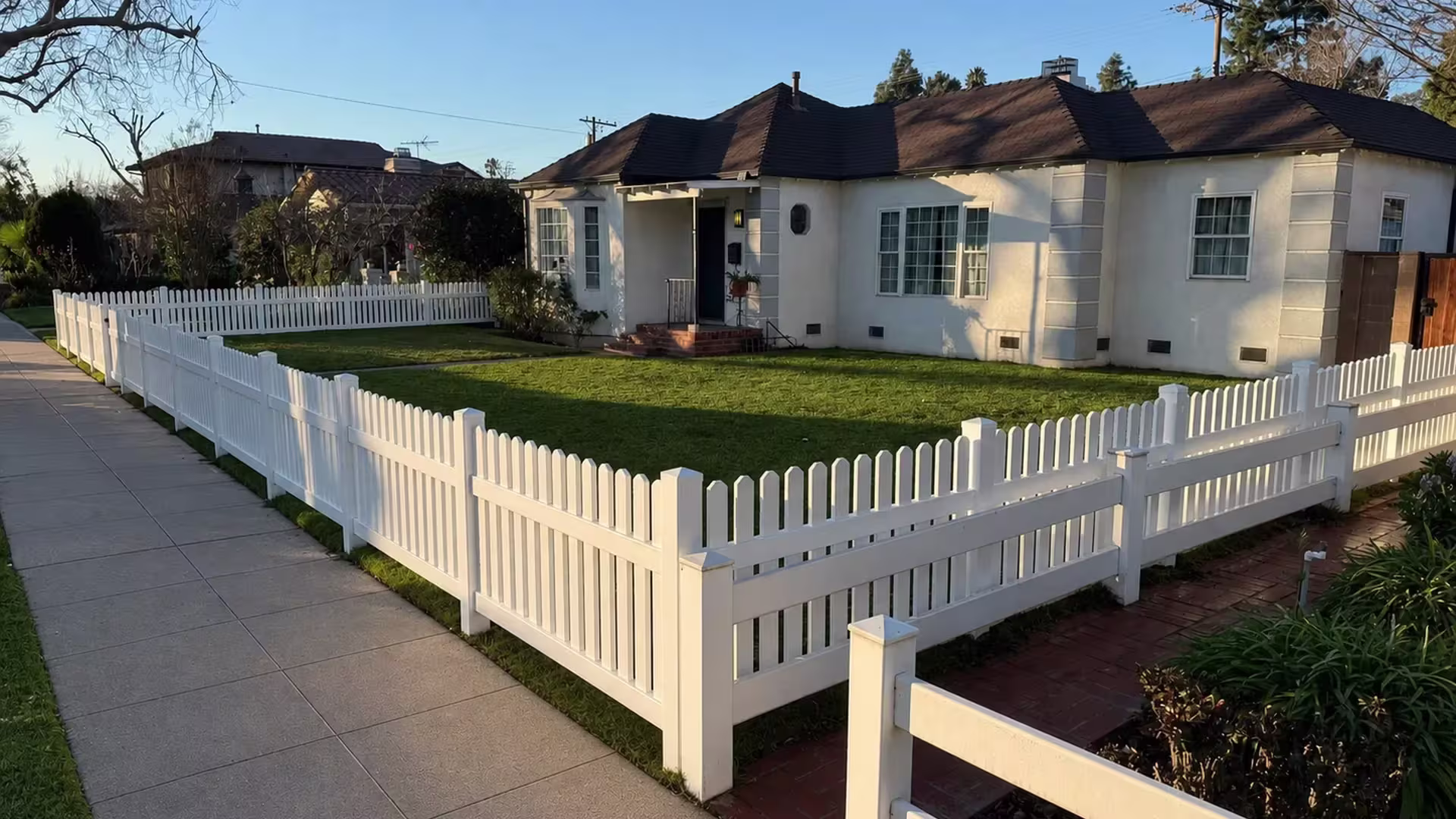 Every corner of the front lawn is enclosed by this White vinyl picket fence circling a stucco house