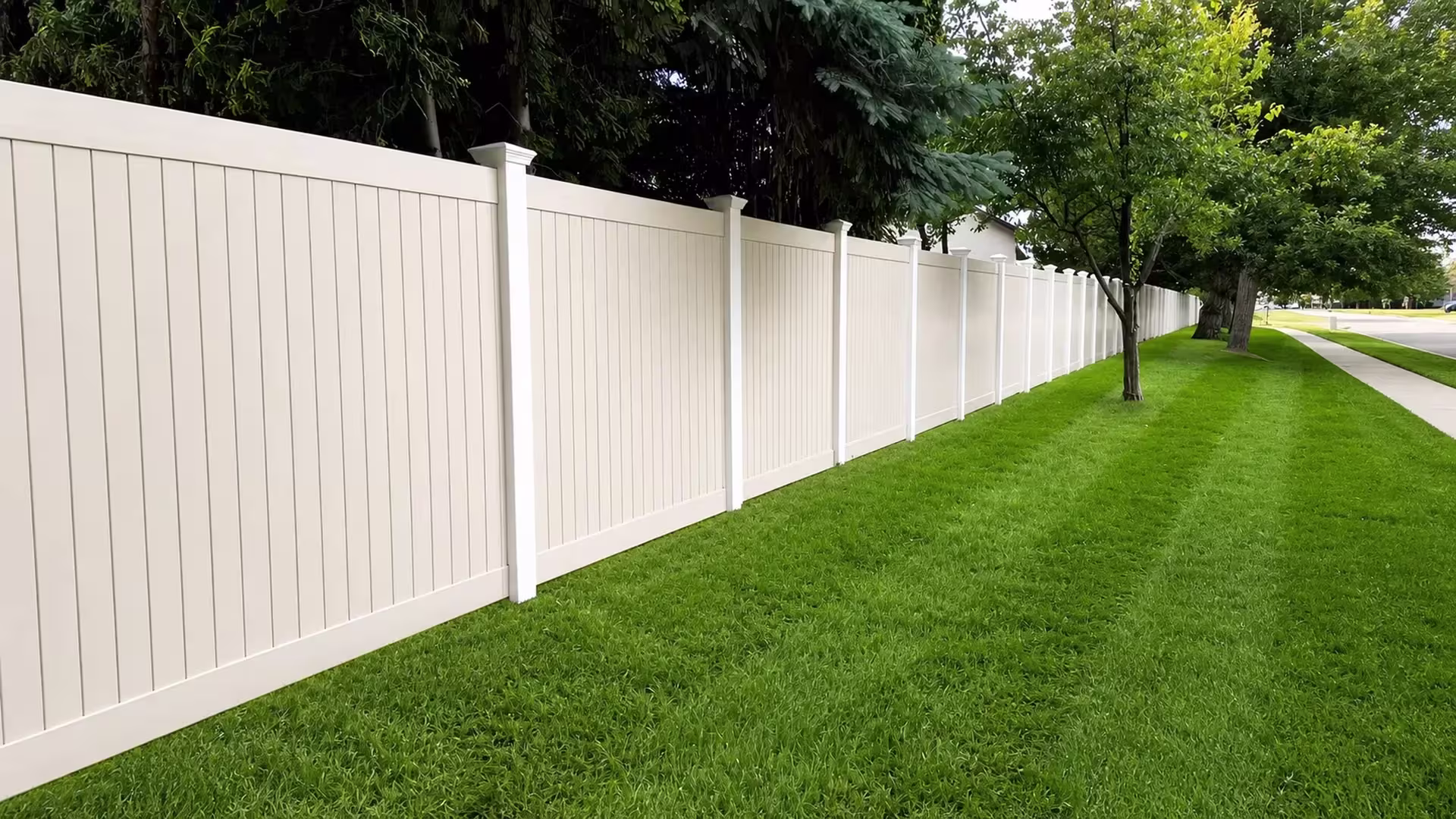 Ivory vinyl two-tone fence extending past a sidewalk toward the street edge