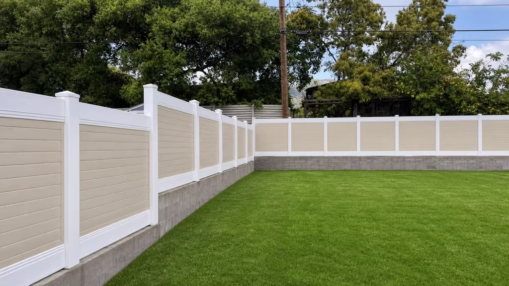 Beige vinyl two-tone fence enclosing two sides of a lawn above a masonry base