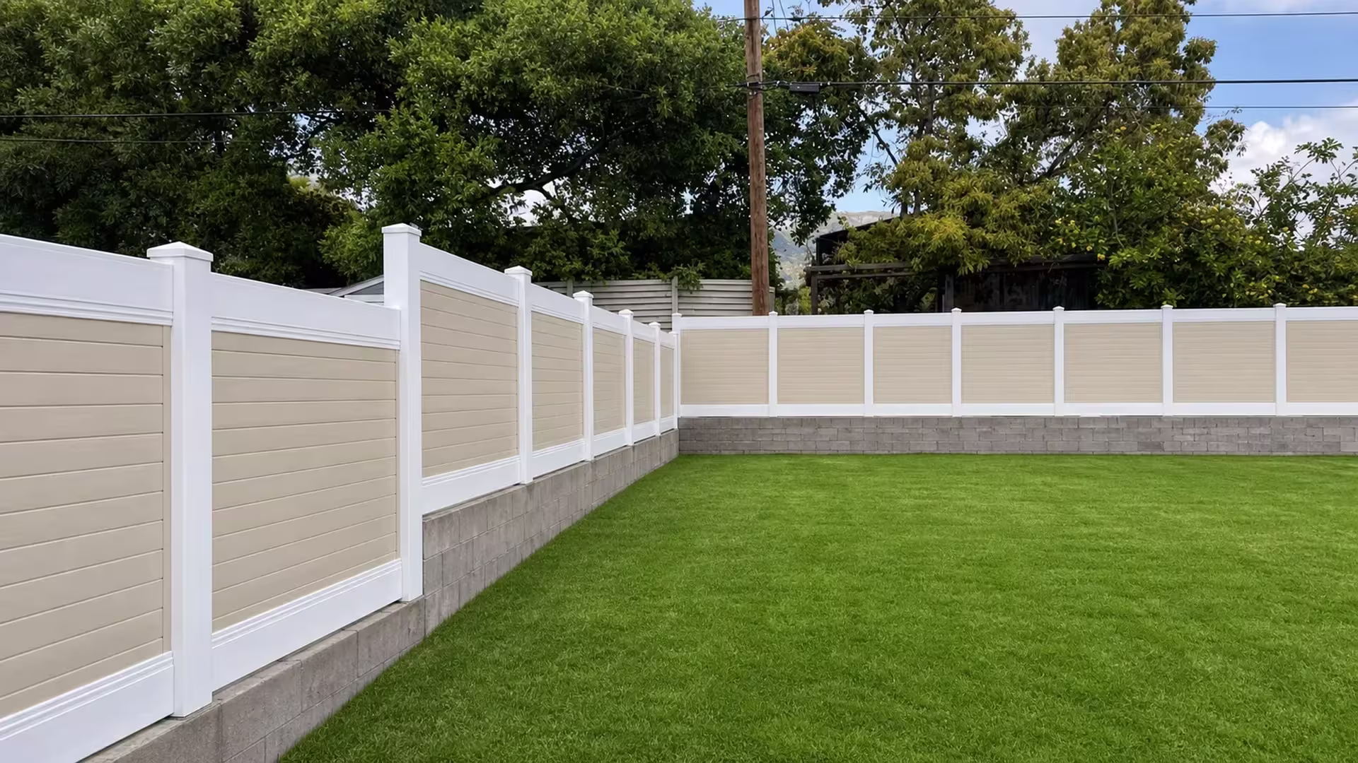Beige vinyl two-tone fence enclosing two sides of a lawn above a masonry base