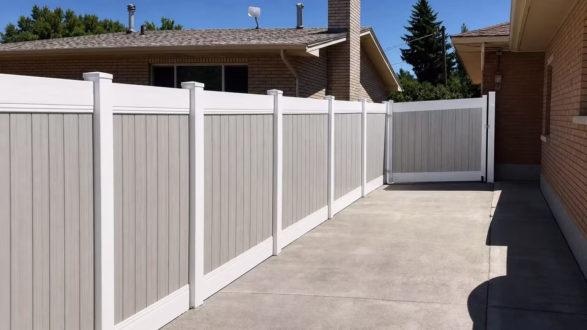 The concrete driveway leads to a gate set in the White vinyl two-tone fence