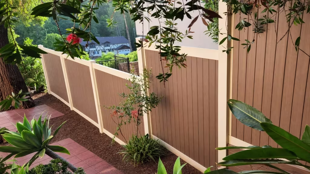 Cream vinyl two-tone fence with brown woodgrain boards stepping through a planted hillside yard