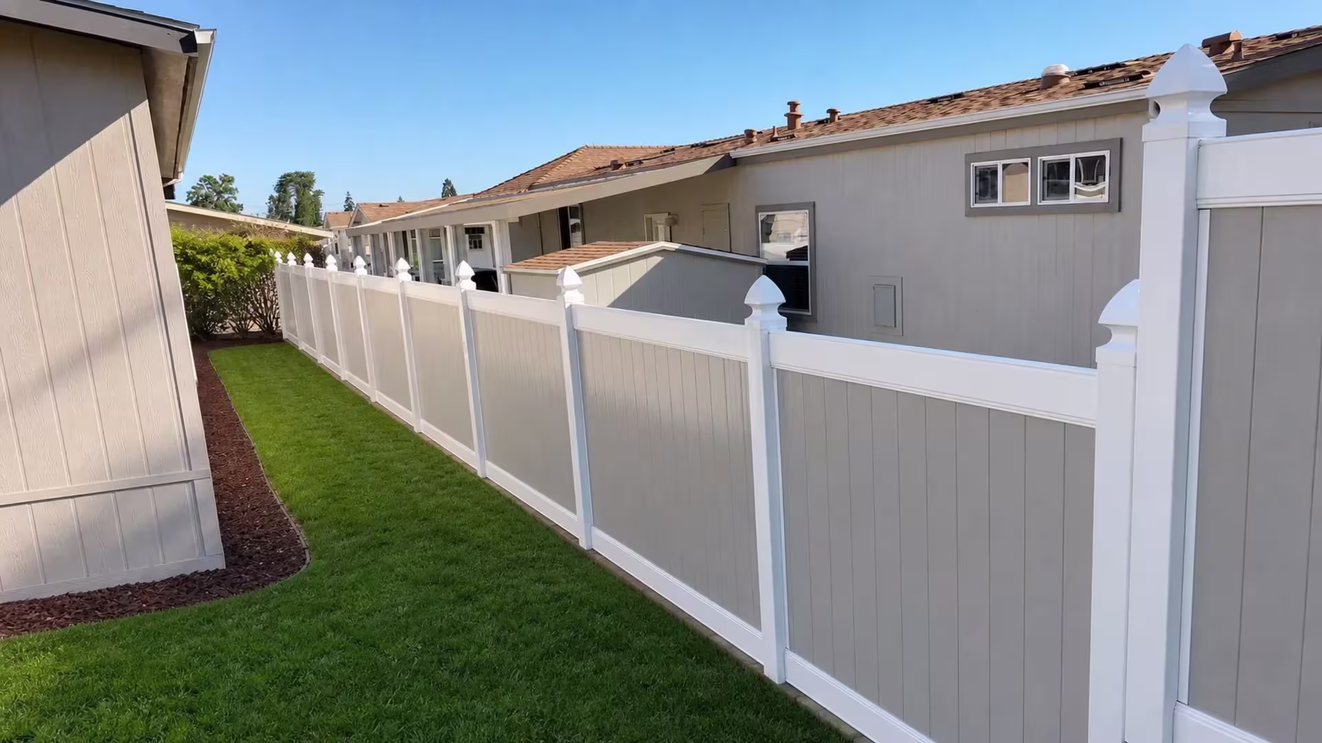 Pointed decorative post caps top a White vinyl two-tone fence running diagonally past a mulch strip