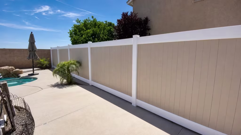 A concrete pool deck and neighboring masonry wall border a Beige vinyl two-tone fence