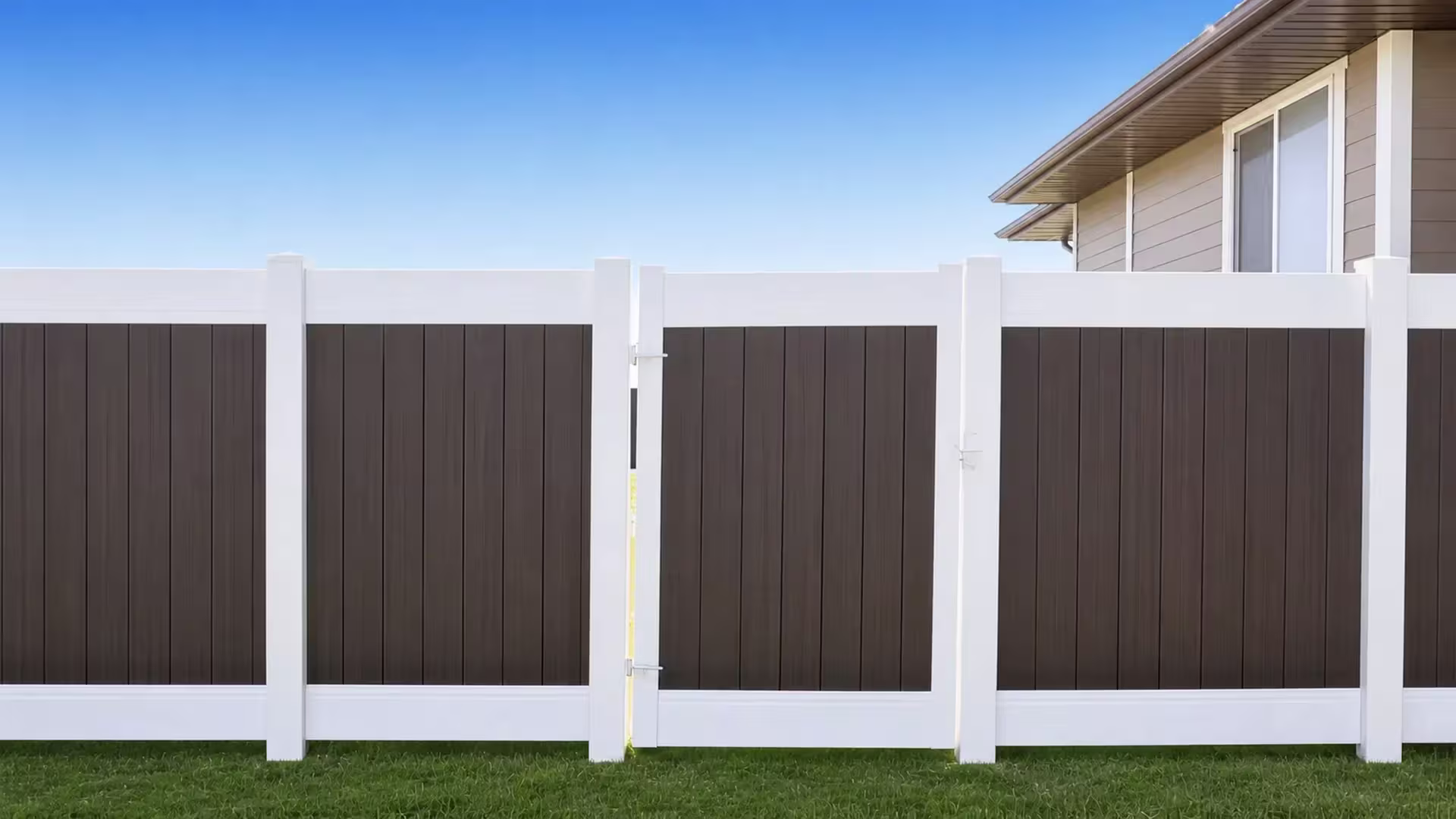 Beige-toned vinyl two-tone fence with a gate standing beside a stucco house and lawn