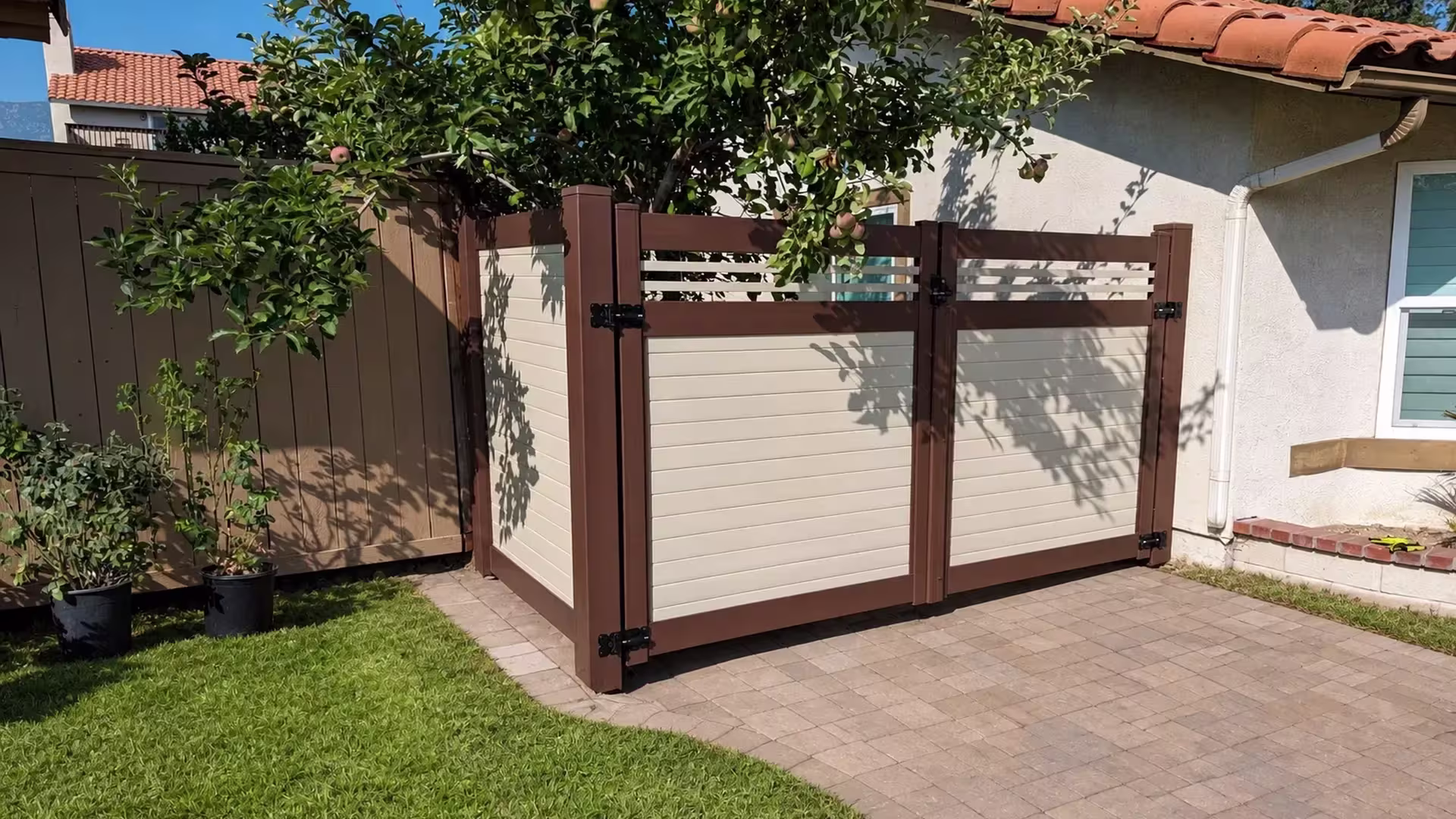 An angled return panel joins this Beige two-tone vinyl driveway gate beside potted plants