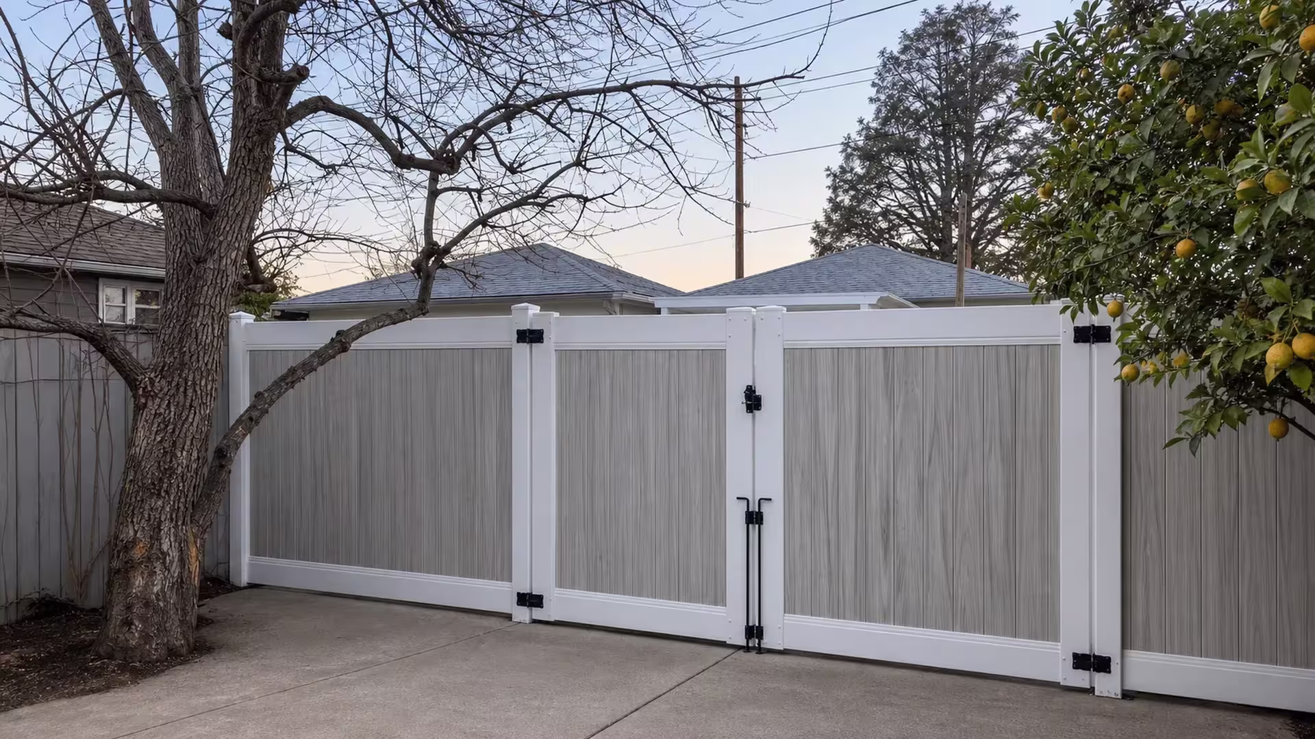 Three broad gray woodgrain panels fill this White two-tone vinyl driveway gate beneath a bare tree