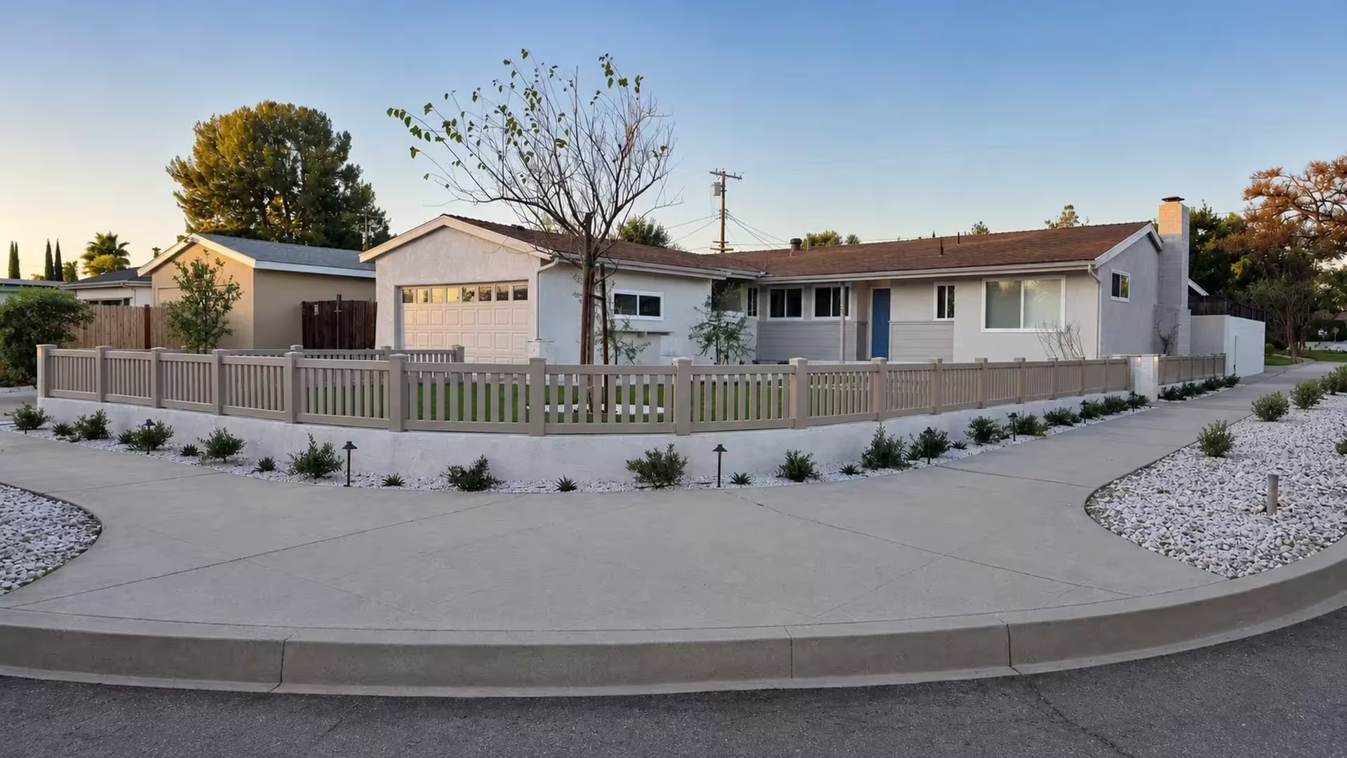 A low white stucco wall carries this Clay vinyl fence, closed-top pickets, around a corner-lot front yard