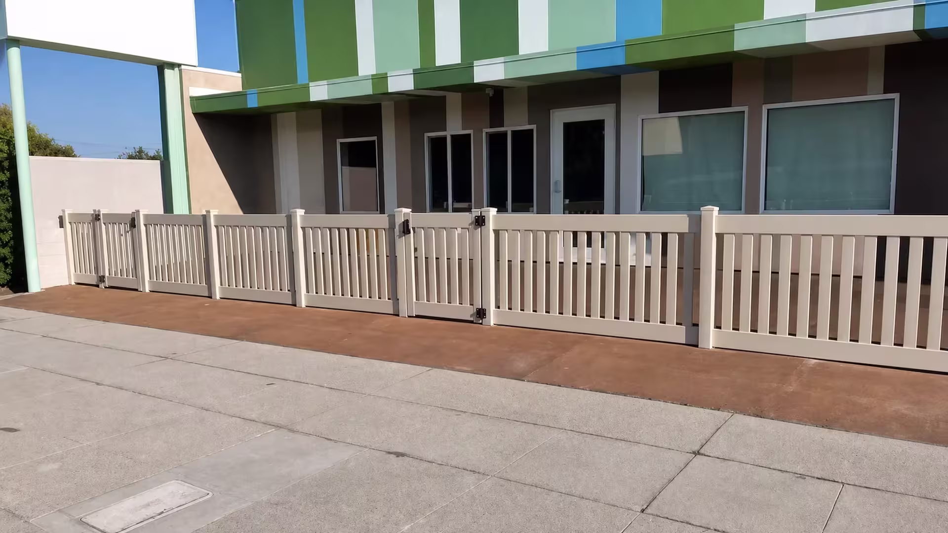 A Clay vinyl closed-top picket fence fronts a commercial storefront, six posts with beveled caps under a striped awning