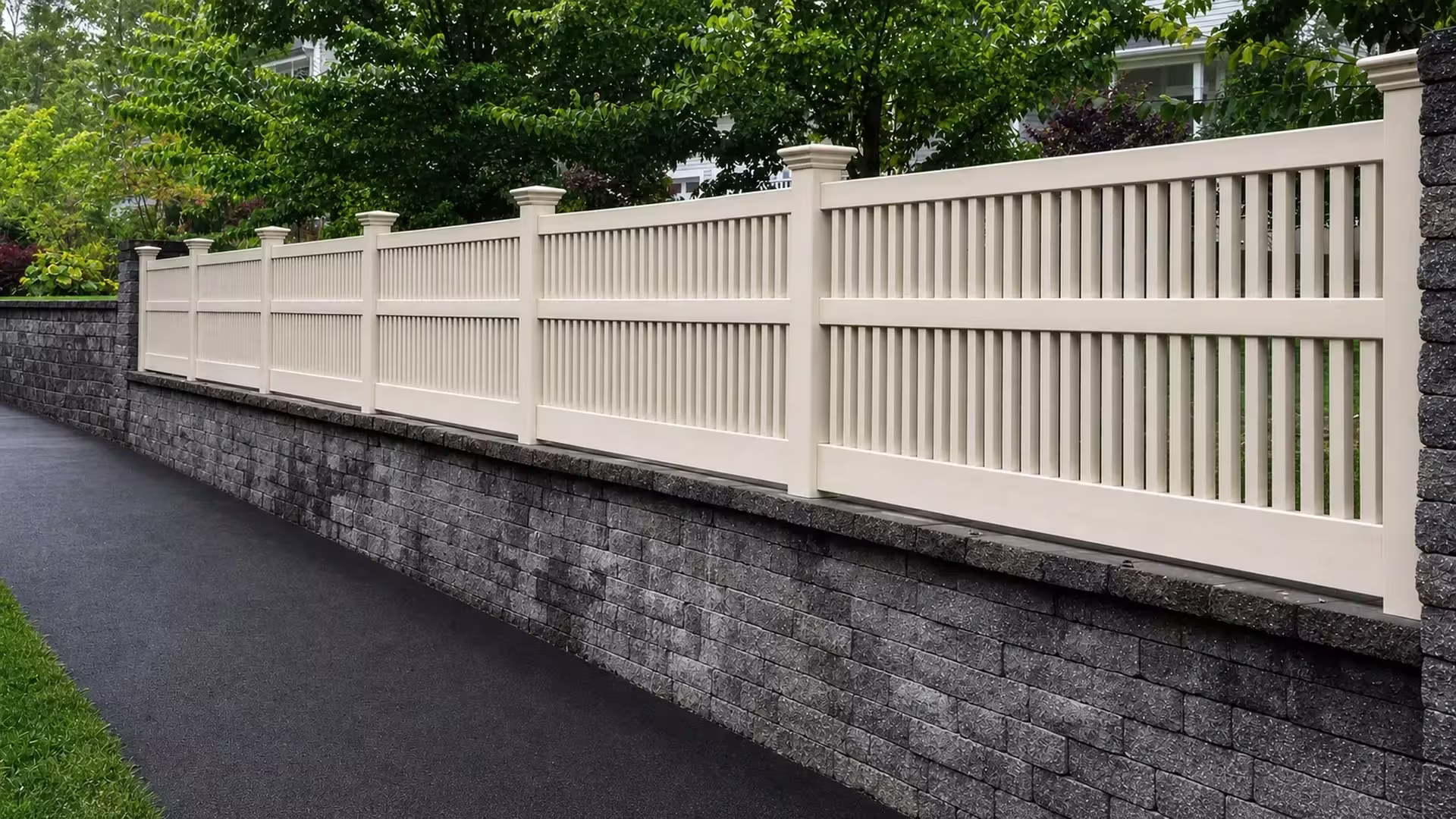 Tan vinyl fence pickets, closed at the top, step along the cap of a gray block retaining wall