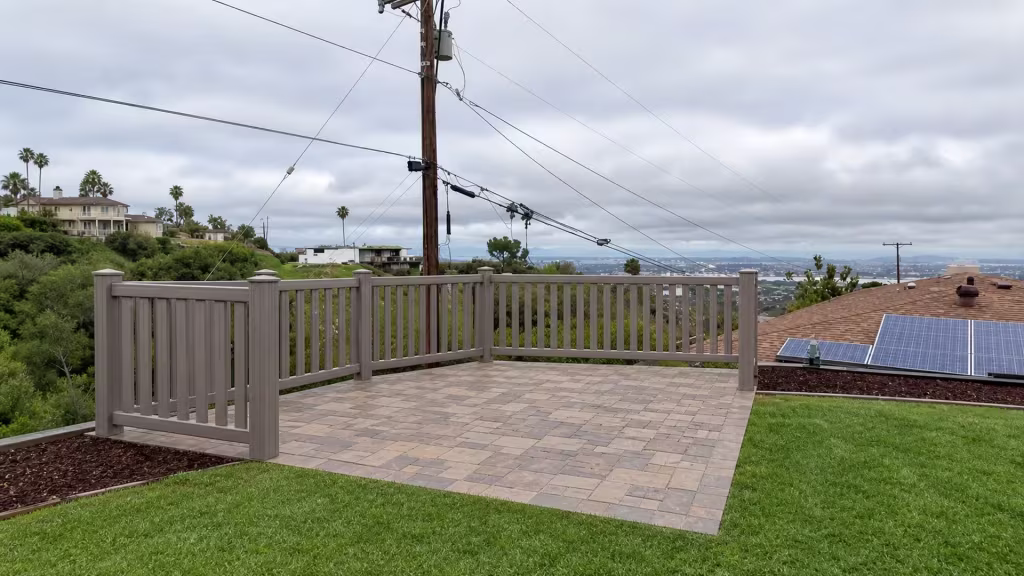 A Weathered Blend vinyl fence of closed-top pickets wraps a hillside patio beneath a rooftop solar array