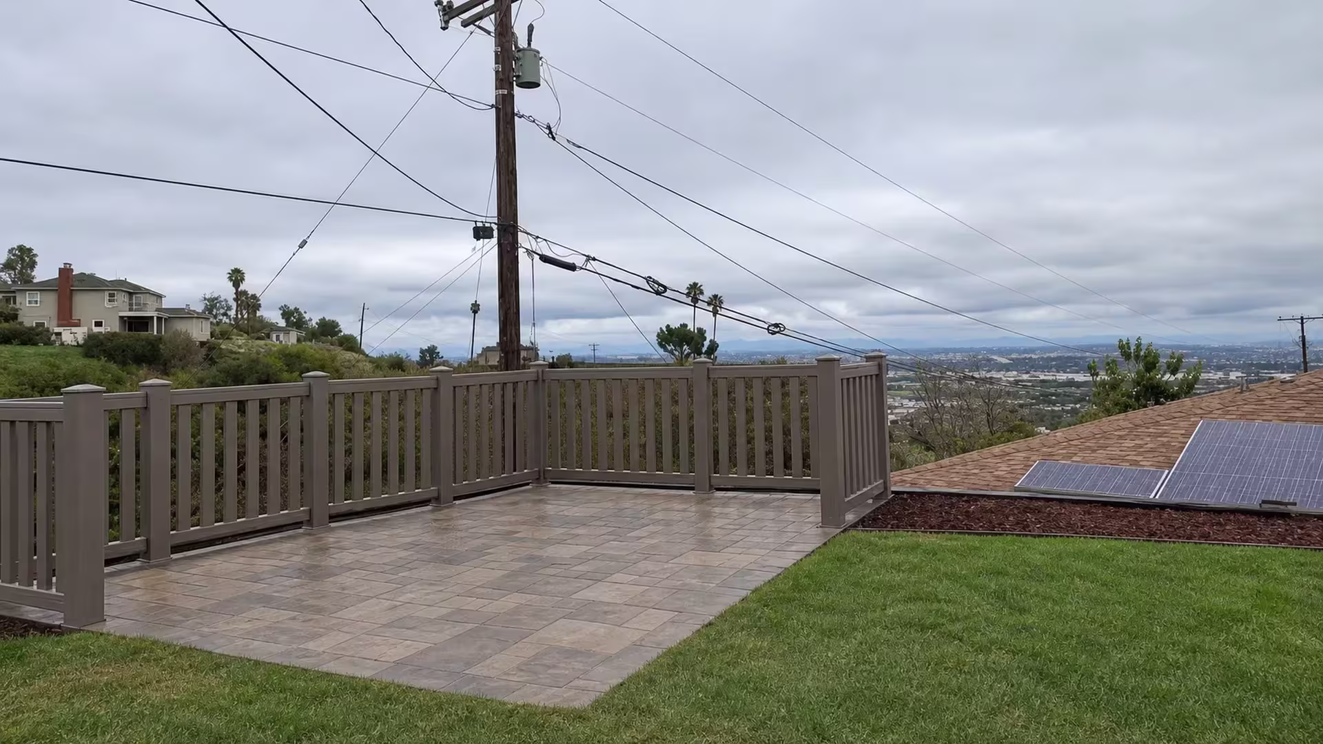 Broad rails carry a Weathered Blend vinyl closed-top picket fence around a stone-paved terrace below distant hills