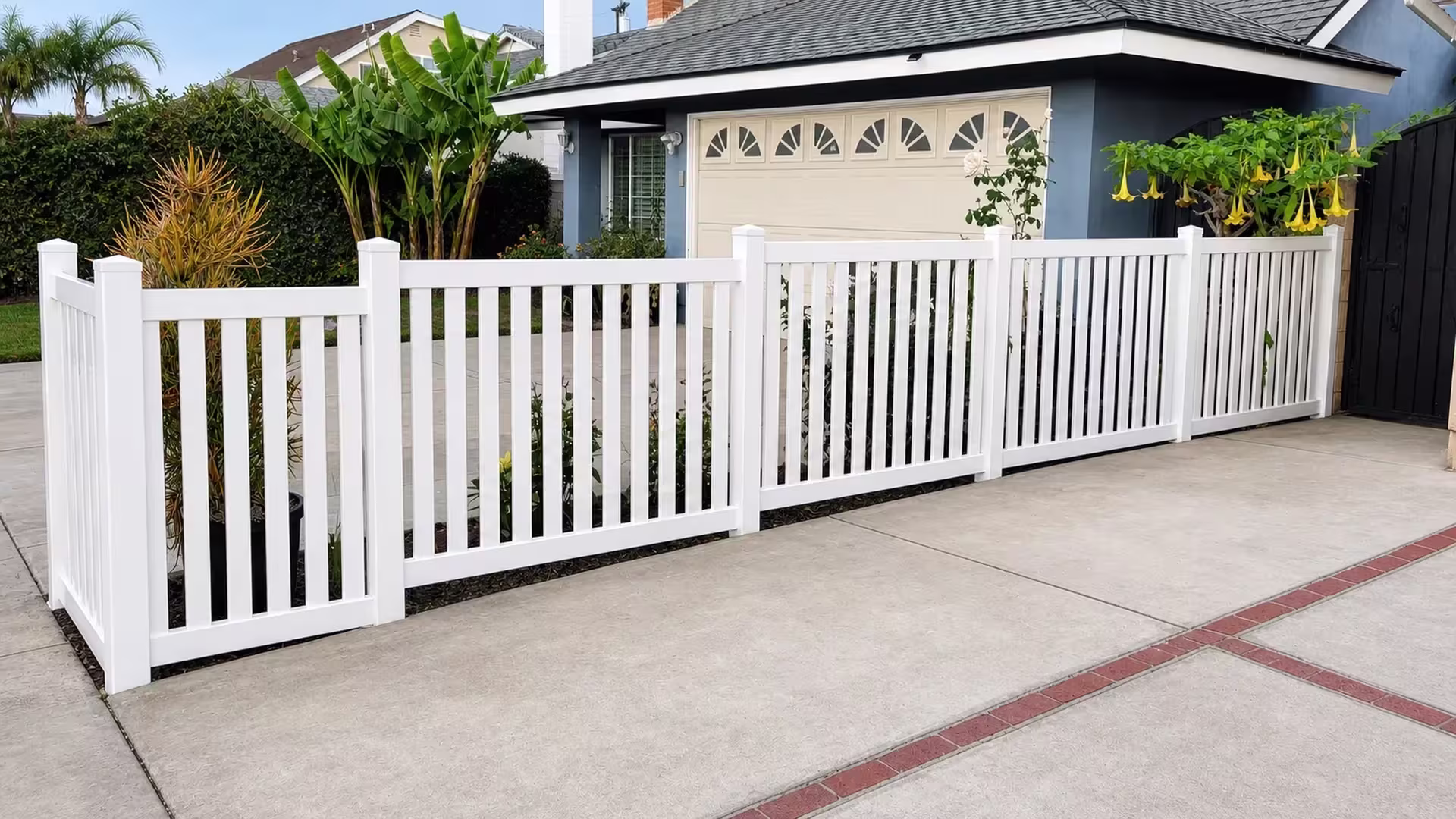 A brick border leads the closed-top picket run, White and vinyl, to a fence line beside a darker side fence