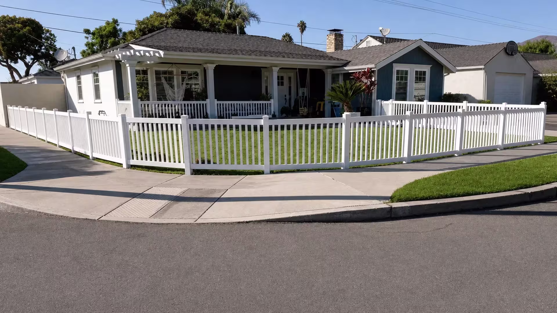 Two runs of White vinyl picket fence meet at a corner, one along the front walkway and one facing the street
