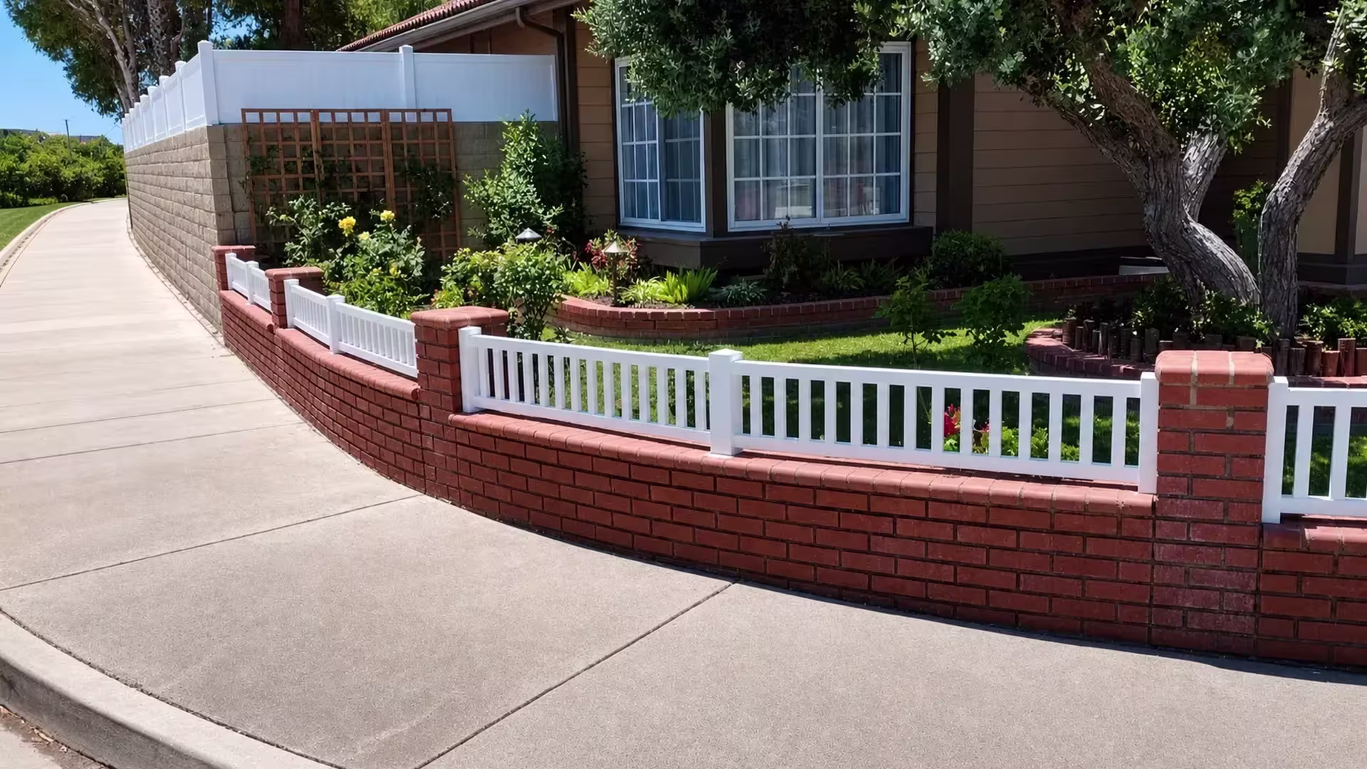 White vinyl picket fence, closed at the top, follows a curved brick wall between masonry piers and coping
