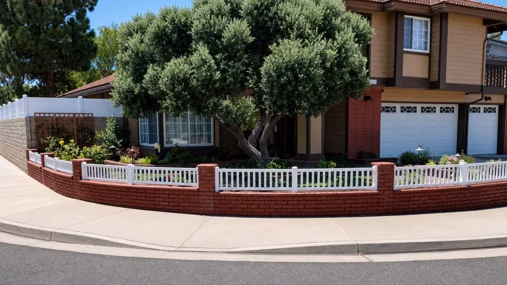 A curved brick wall carries this White vinyl picket fence past the garage, driveway and a planted front garden