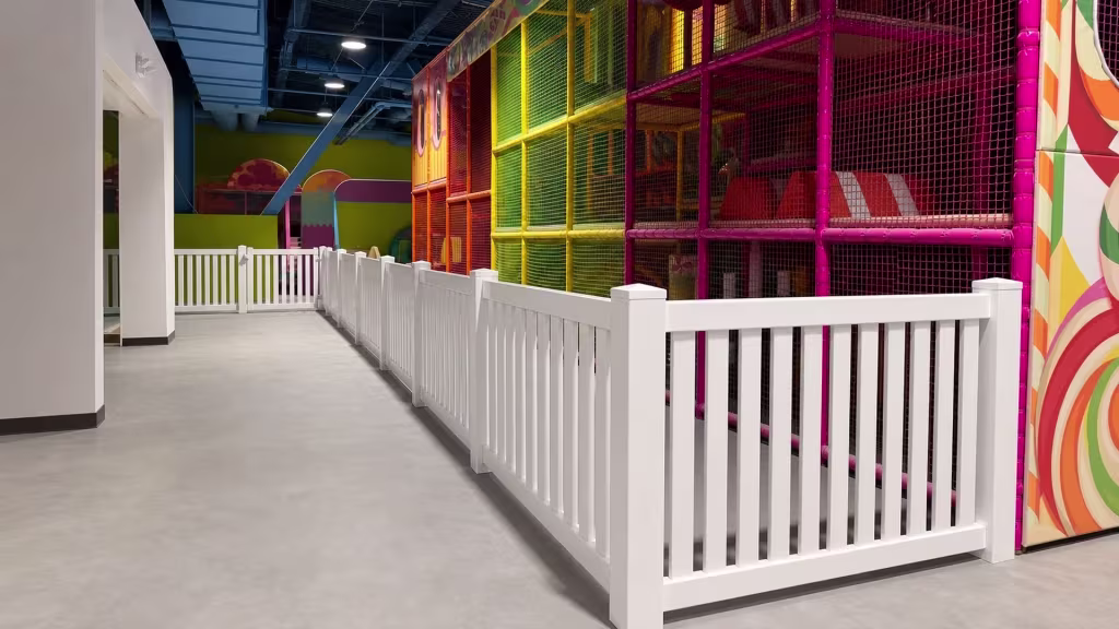An L-shaped run of White vinyl picket fence forms part of an indoor children's play facility