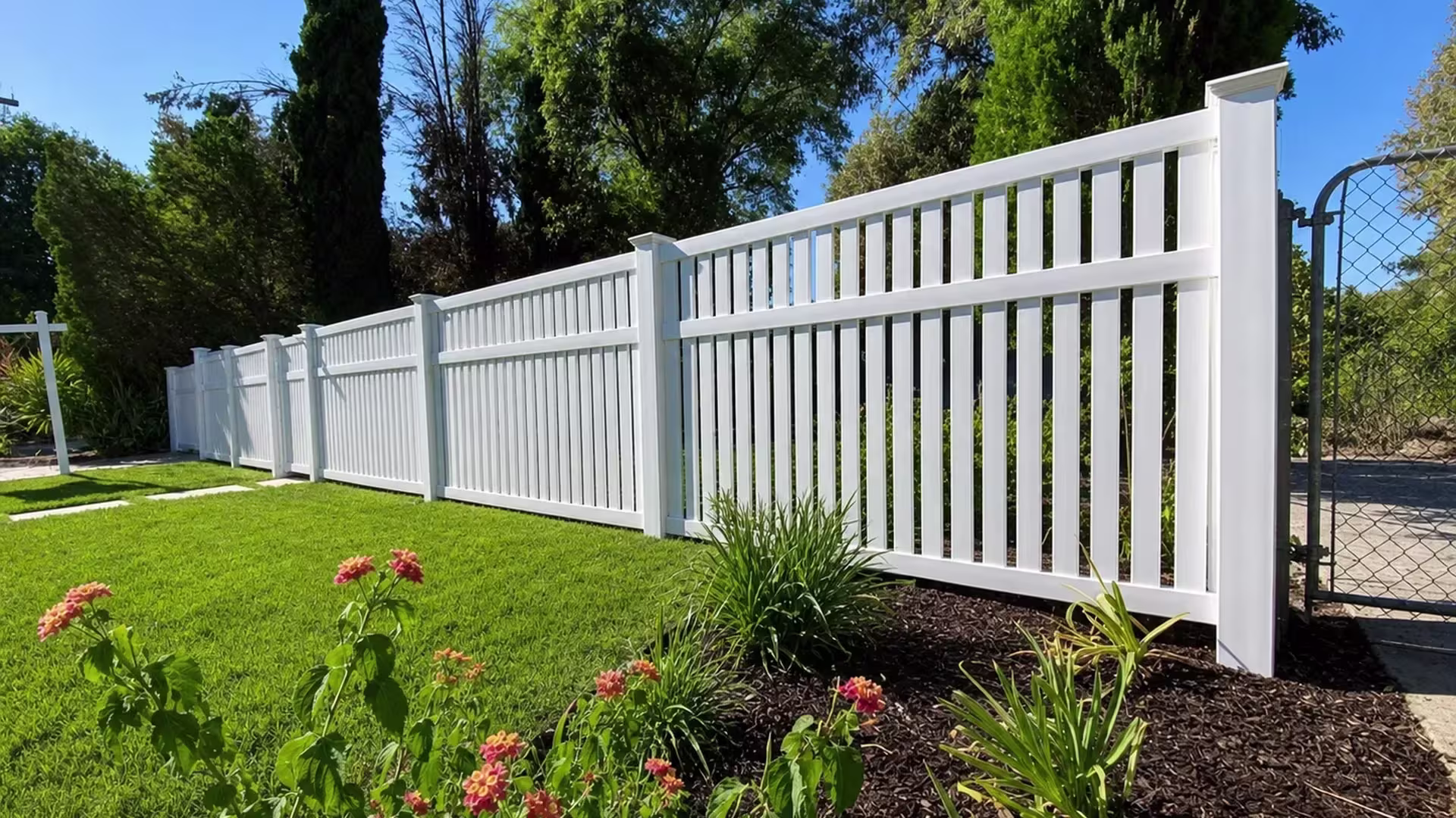 This White vinyl picket fence steps down in height, taller panels giving way to lower sections with solid board bases
