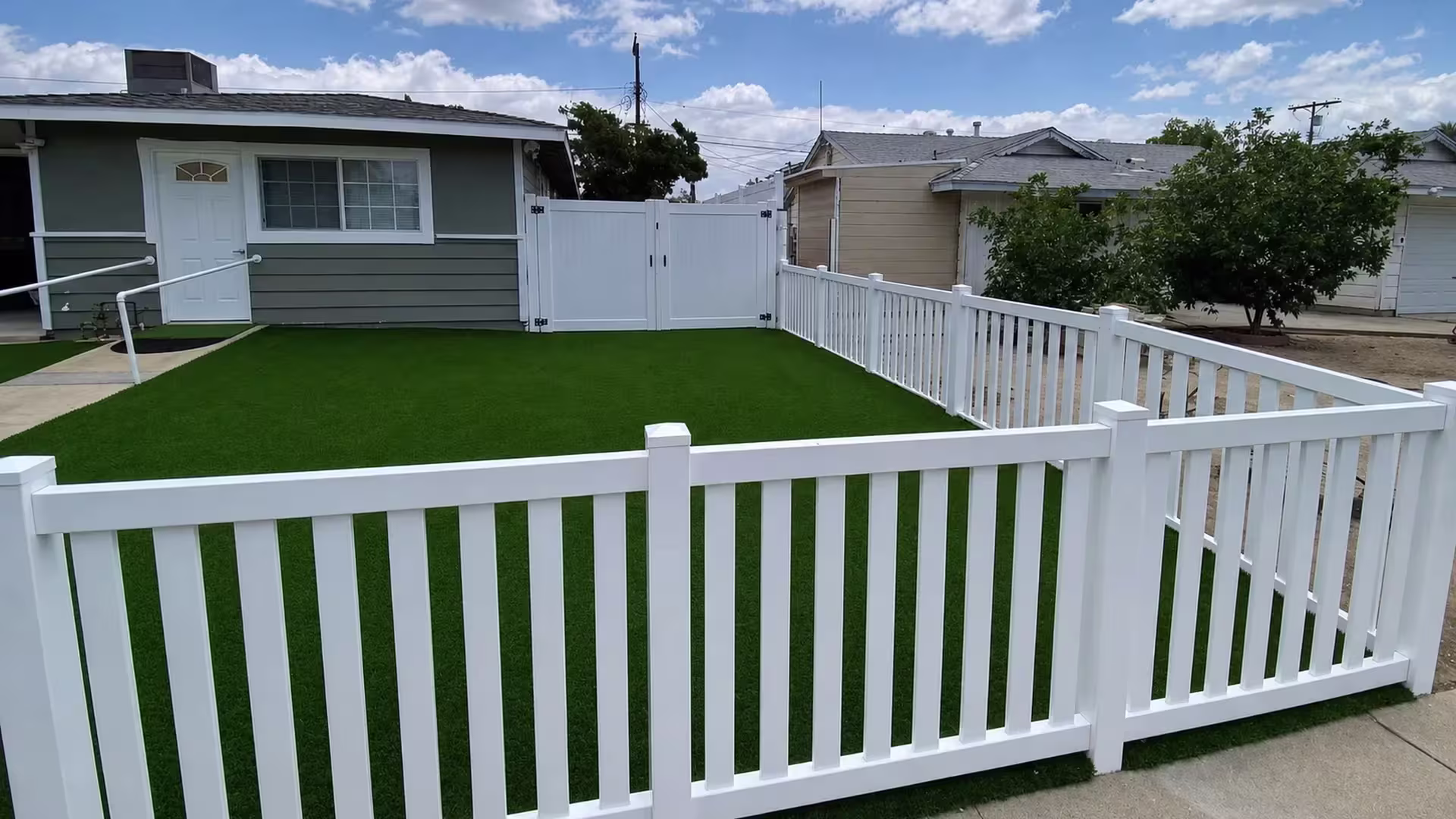 Several angled turns carry this White vinyl picket fence around a rectangular artificial-turf yard beside a gray house