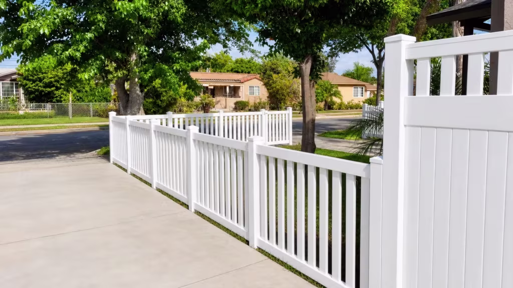 Under a citrus tree with fruit, the corner picket fence turns White and vinyl with a closed top around the lawn