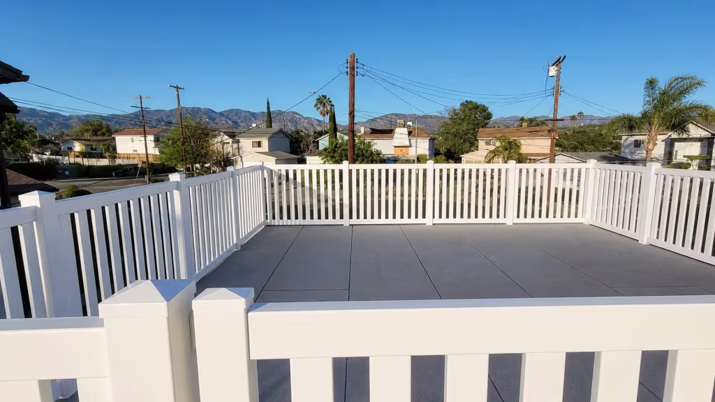 Control-joint lines score the patio slab that a White vinyl picket fence rings in a U shape
