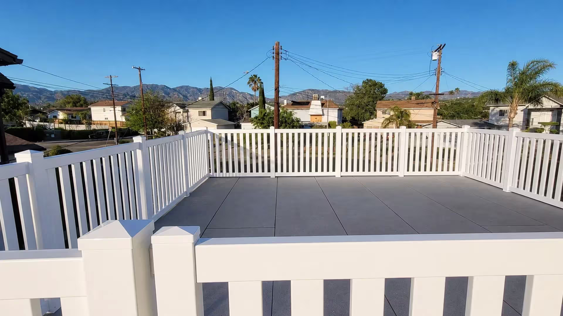 Control-joint lines score the patio slab that a White vinyl picket fence rings in a U shape