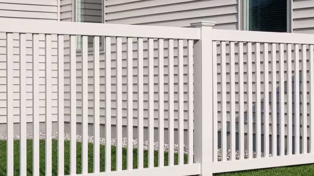 One decorative center post divides two inline White vinyl fence sections with closed-top pickets before a beige-sided house
