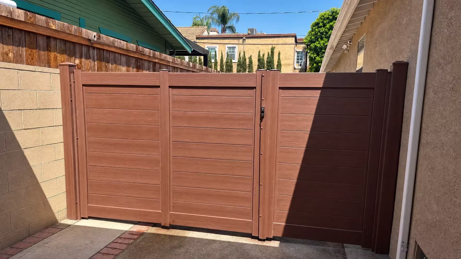 Two gate leaves in Brazilian Blend vinyl privacy fence close a driveway edged with brick and a masonry wall