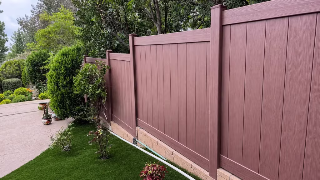 Five posts step down a sloped garden in this Brazilian Blend vinyl privacy fence beside a tan brick base wall